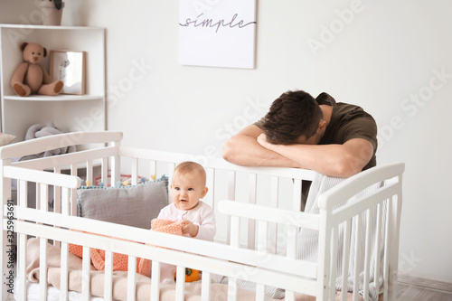 Fotografie Young man suffering from postnatal depression near bed with baby at home