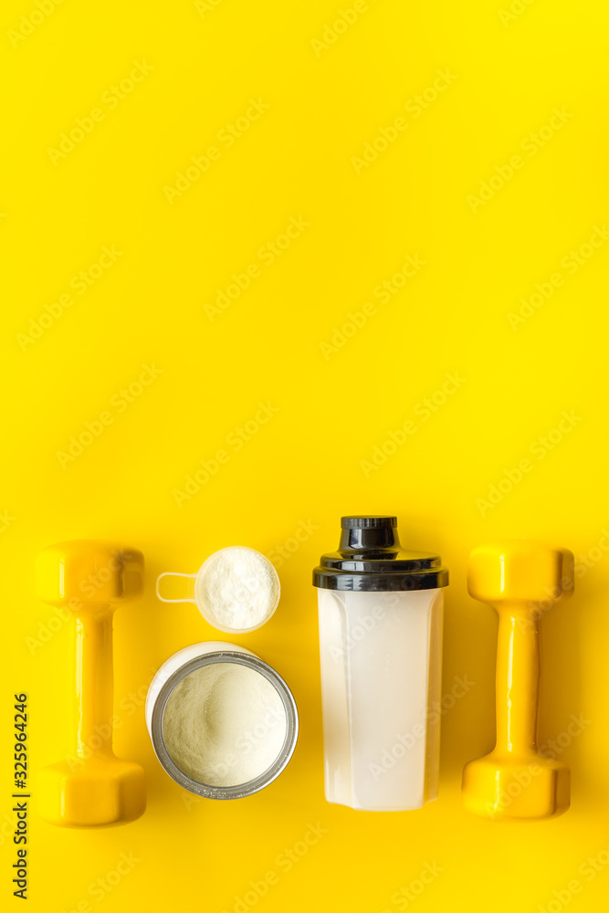 Sport nutrition. Whey protein, shaker, dumbbells on yellow background top-down flay lay copy space Sport nutrition. Whey protein, shaker, dumbbells on yellow background top-down flay lay copy space