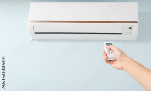 Male technician with remote control checking operation of air conditioner indoors