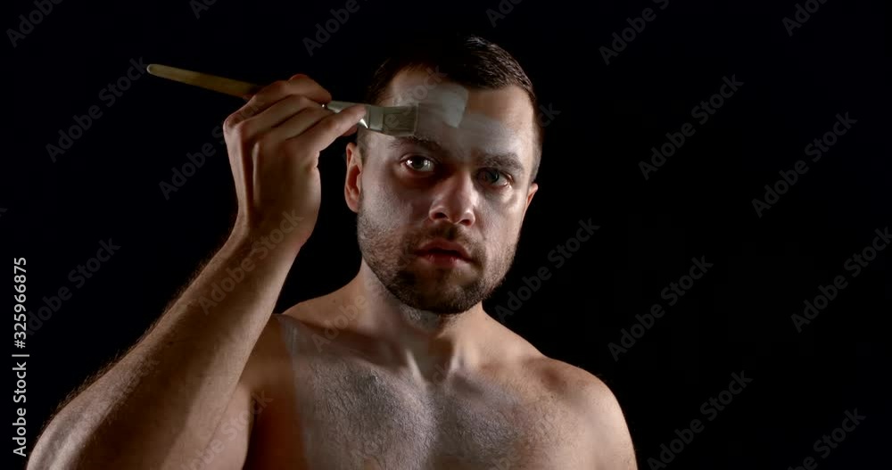 male actor is covering his face by white greasepaint using brush in dark room male actor is covering his face by white greasepaint using brush in dark room