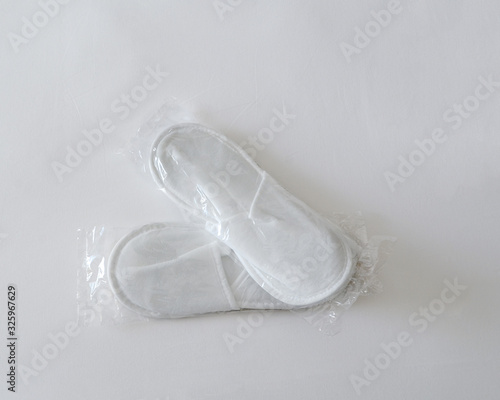 New white disposable slippers in a transparent package lie on white bedsheet