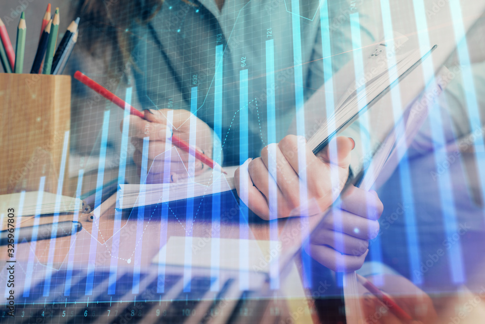 A woman hands writing information about stock market in notepad. Forex chart holograms in front. Concept of research. Multi exposure A woman hands writing information about stock market in notepad. Forex chart holograms in front. Concept of research. Multi exposure