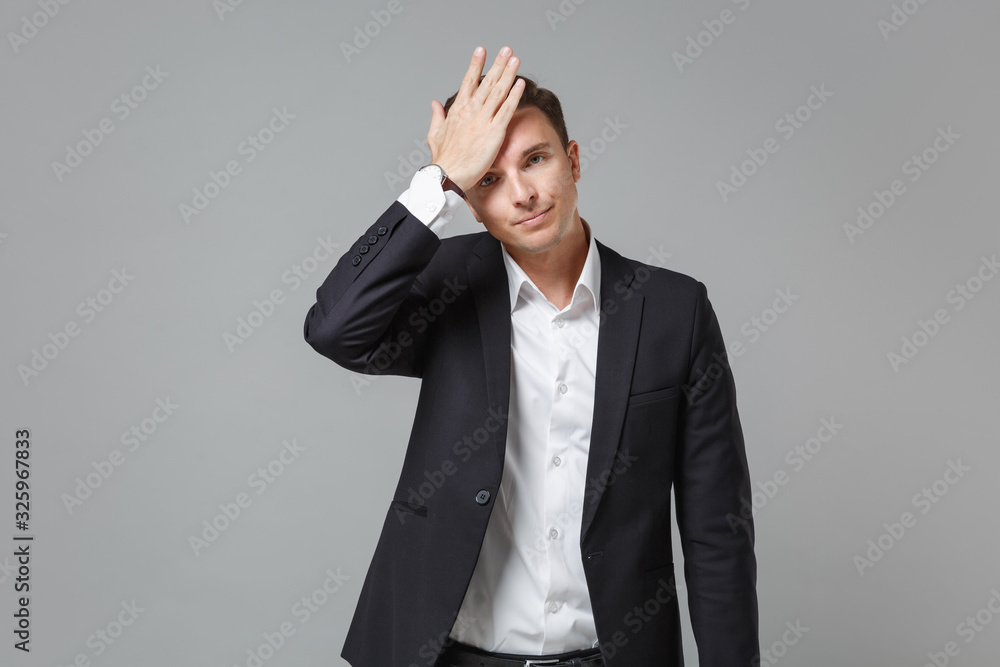 Tired young business man in classic black suit shirt posing isolated on grey wall background studio portrait. Achievement career wealth business concept. Mock up copy space. Put hand on head, face.