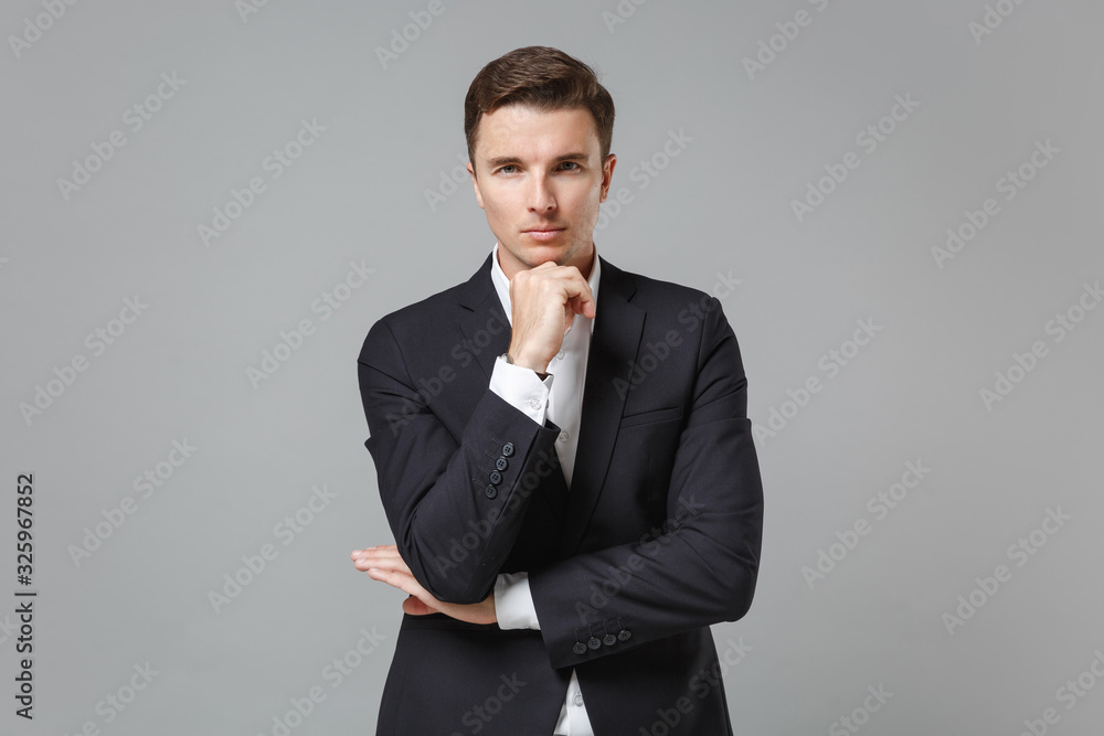 Successful young business man in classic black suit shirt posing isolated on grey background studio portrait. Achievement career wealth business concept. Mock up copy space. Put hand prop up on chin. Successful young business man in classic black suit shirt posing isolated on grey background studio portrait. Achievement career wealth business concept. Mock up copy space. Put hand prop up on chin.