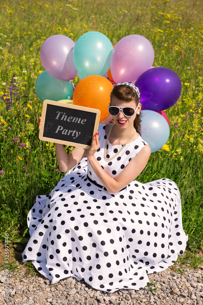 Woman with a rock n Roll dress and balloons holding a slate with text theme party foto de Stock Adobe Stock