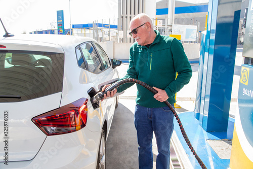 Older man filling up with gas in his eco-friendly car.
