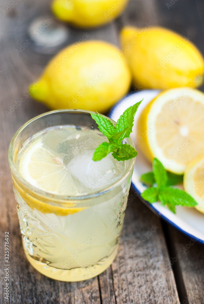 Glass with fresh lemonade on a wooden table with lemons in the background Glass with fresh lemonade on a wooden table with lemons in the background