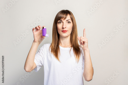 young woman holds in her hand an inhaler, holding thumbs up on a light background. Banner. Concept for easier breathing, treatment of asthma, pharynx, larynx, trachea