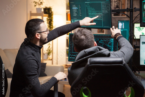 Back view of hackers pointing on computer screens