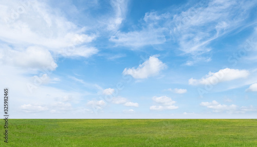 Green grass field and blue sky with white clouds. Beautiful landscape background.