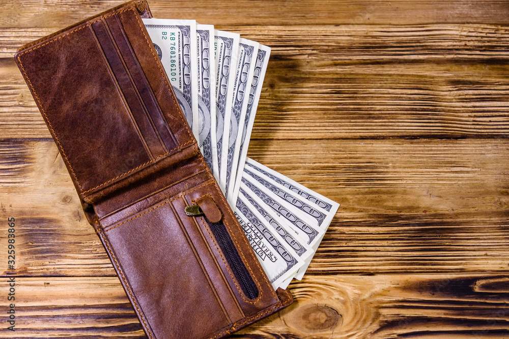 Brown leather wallet and one hundred dollar banknotes on the wooden background