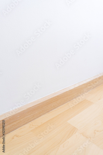 Wooden wall base skirting, finishing material with wood laminate floor and white mortar wall. Empty room with white wall and wooden floor.