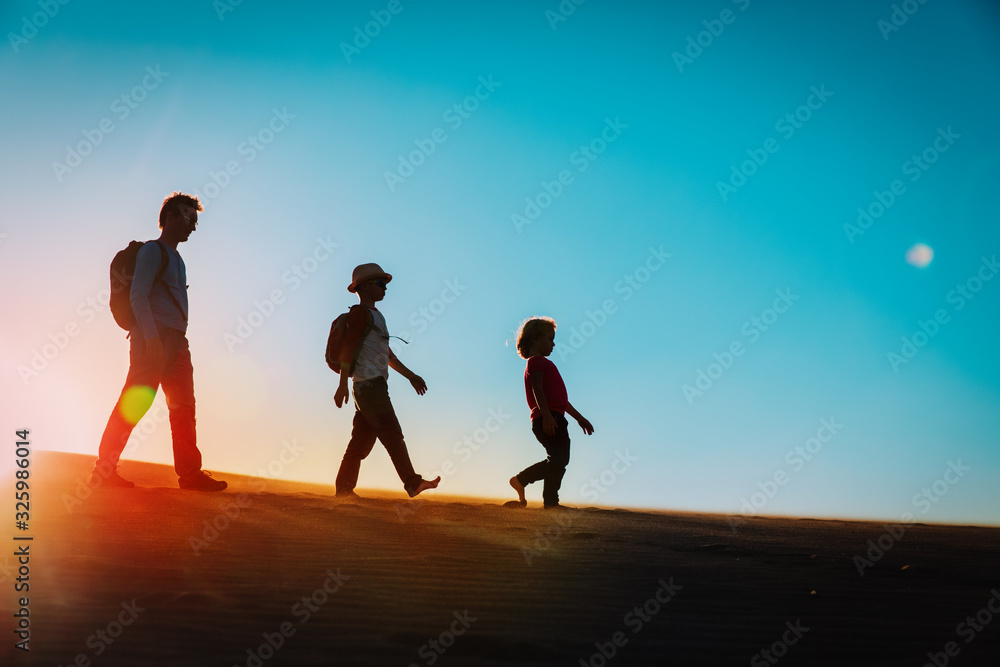 Silhouettes of father with son and daughter hiking at sunset