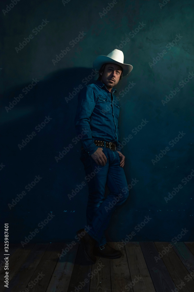 Man wearing denim shirt and cowboy hat standing against wall. Man wearing denim shirt and cowboy hat standing against wall.