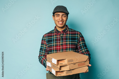 Cheerful happy egyptian man from delievery serive posing on camera and smile. Hold pizza boxes in hands. Guy in checkered shirt look straight. Isolated over blue background. photo