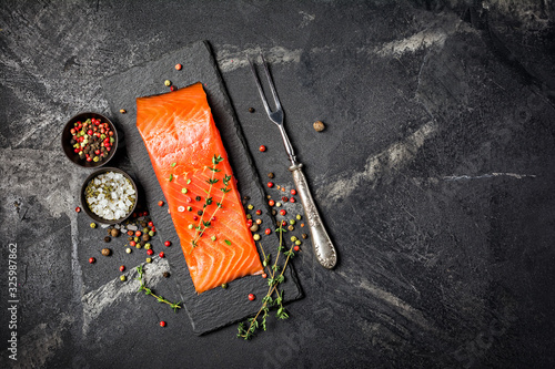 Piece of red fish fillet with spices on black slate board with vintage silver fork photo