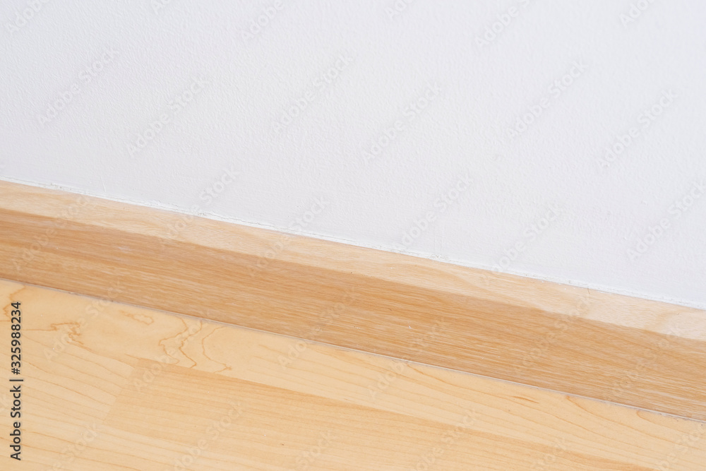 Wooden wall base skirting, finishing material with wood laminate floor and white mortar wall. Empty room with white wall and wooden floor. Wooden wall base skirting, finishing material with wood laminate floor and white mortar wall. Empty room with white wall and wooden floor.