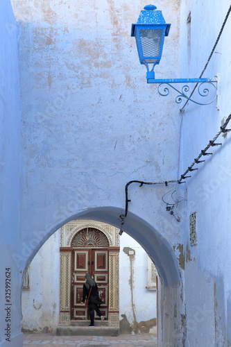 Typical narrow streets inside the historical medina of Kairouan in Tunisia, with blue colors and a traditional wooden door viewed through an arcade