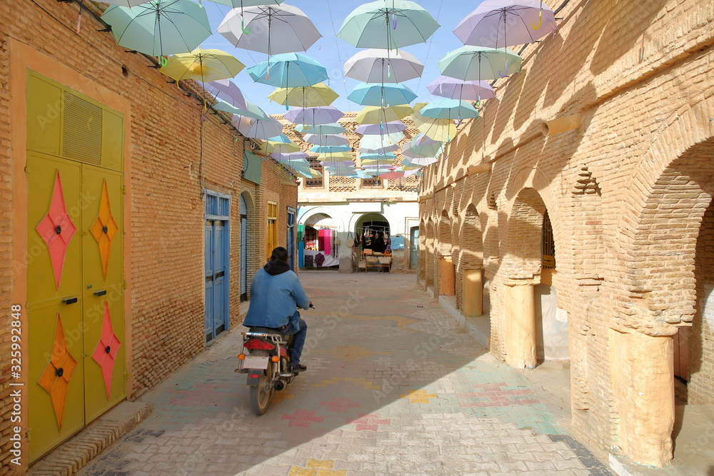 Obraz premium Typical cobbled and narrow street inside the medina of Nefta, Tunisia, with colorful umbrellas and doors