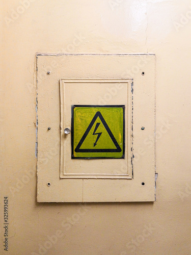 Locked electrical panel on the wall painted with yellow oil paint. There is a high voltage sign on the door. © Nekrasov