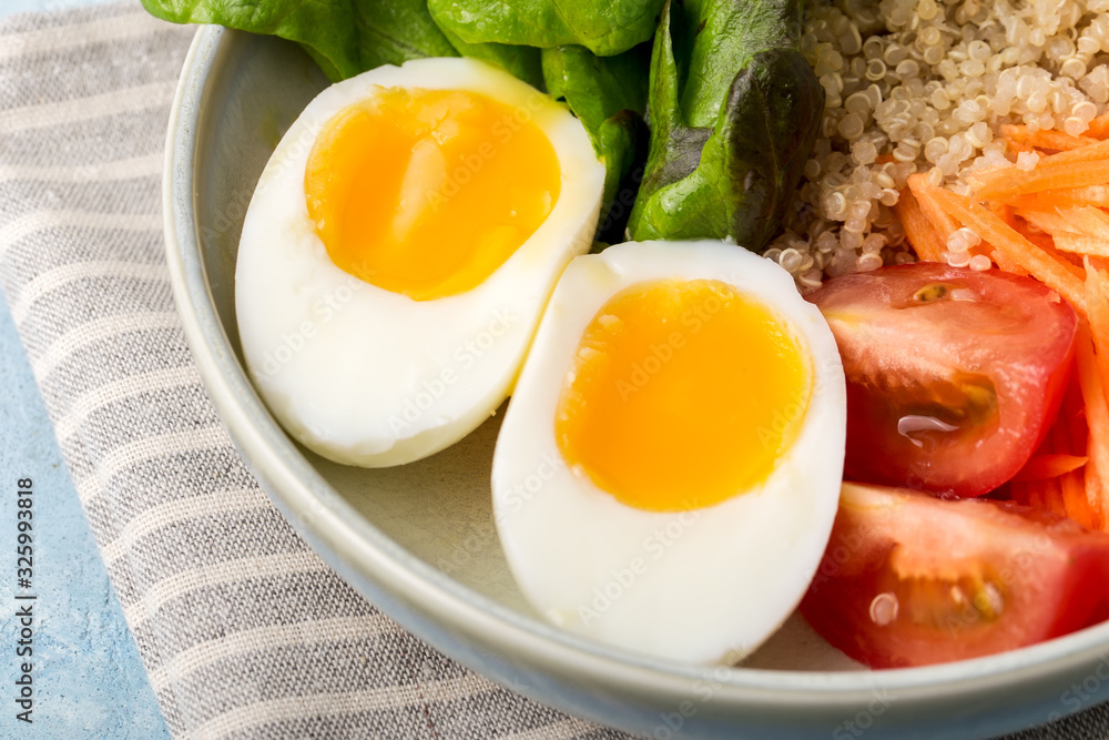 Healthy green vegetarian buddha bowl lunch with eggs, quinoa, carrots,tomato, lettuce leaves, on a blue background., close up Healthy green vegetarian buddha bowl lunch with eggs, quinoa, carrots,tomato, lettuce leaves, on a blue background., close up