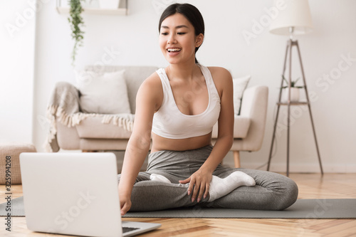 Fototapeta Naklejka Na Ścianę i Meble -  Sport application. Asian girl practicing yoga and using laptop
