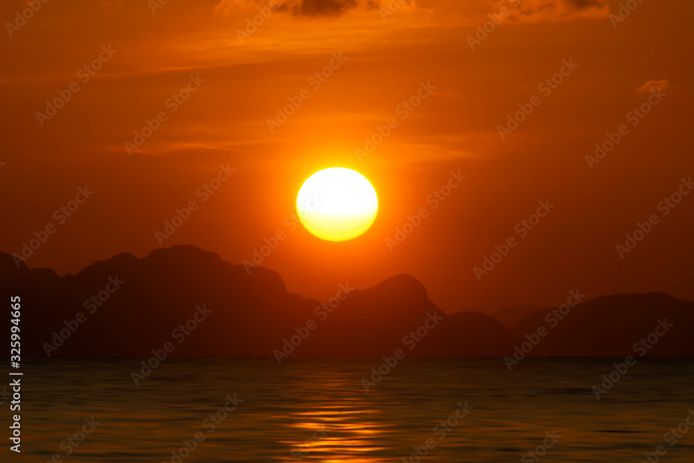 Fototapeta Big sun on sunset sky at the lake with silhouette mountain