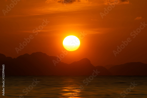 Big sun on sunset sky at the lake with silhouette mountain