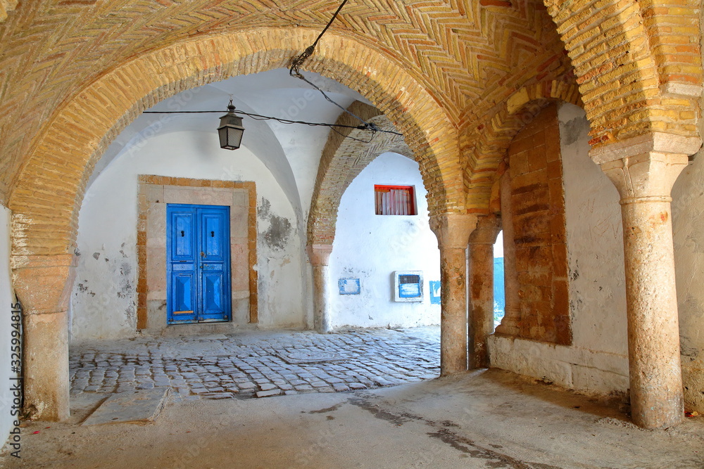 Naklejka premium Typical cobbled and narrow street with colorful doors, columns and arcades inside the historical medina of Tunis, Tunisia