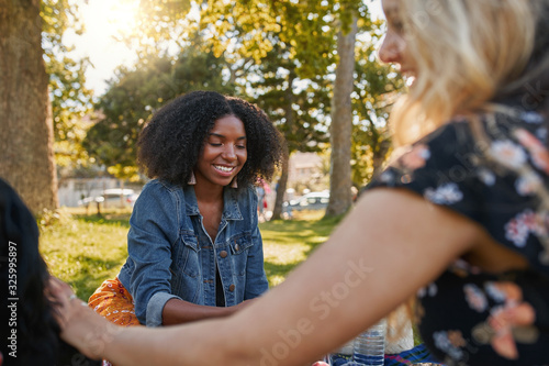 Smiling portrait of a happy african american young woman sitting with her friends in the park having a picnic on a warm summer day