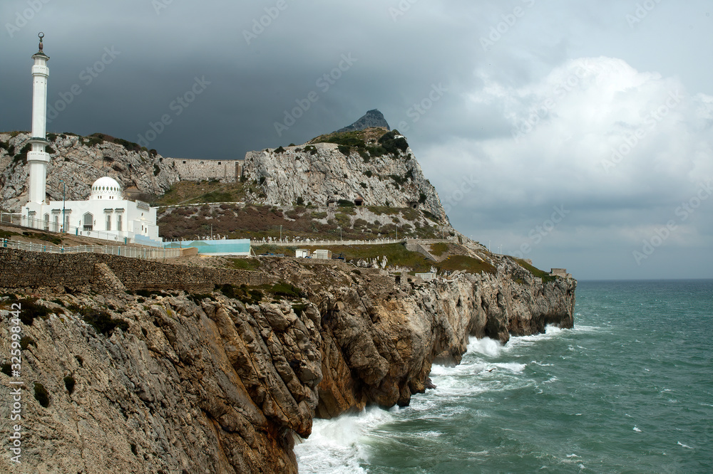 Gibraltar,  view along rugged coastline with mosque against a stormy sky