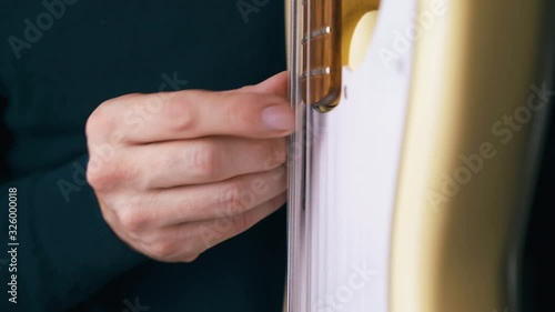 CU: funky artist plays solo on white bass guitar with finger holding instrument in vertical position closeup photo