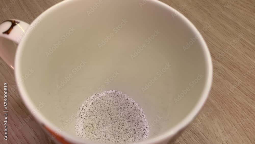 Putting cappuccino powder into a white cup with a spoon. Closeup of white and brown instant coffee particles in a ceramic cup. Making instant capuccino. Putting cappuccino powder into a white cup with a spoon. Closeup of white and brown instant coffee particles in a ceramic cup. Making instant capuccino.