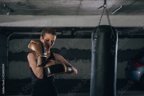 Strong woman with short hair putting on her gold boxing gloves