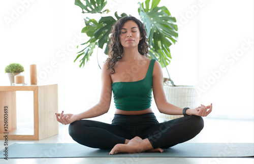 Young Hispanic woman doing meditation in lotus yoga pose at home