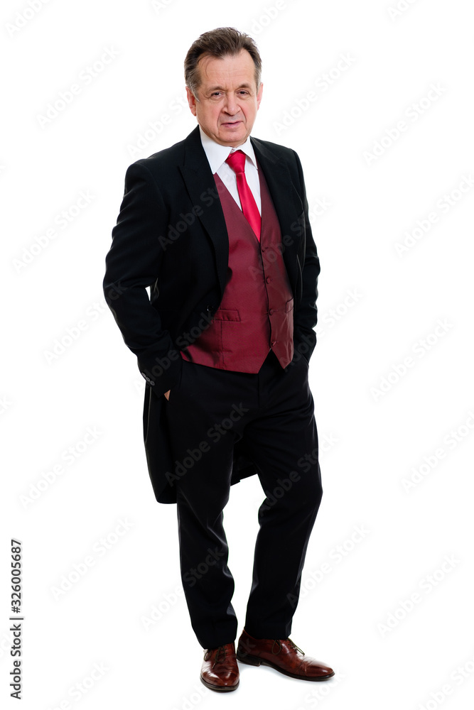 Full lenght Portrait of handsome confident caucasian mature businessman 55-60 years old in black tuxedo and red vest standing with hands in pockets smiling in front on isolated white background. Full lenght Portrait of handsome confident caucasian mature businessman 55-60 years old in black tuxedo and red vest standing with hands in pockets smiling in front on isolated white background.
