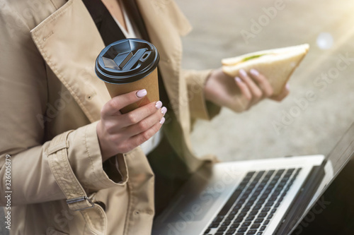 Foto business lady holding laptop on her knees with cup of coffee and sandwich in her