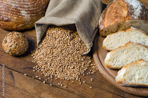 Assortment of bread, ears and grains of wheat in bag on wooden table