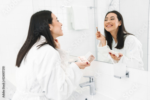 Woman indoors at home in bathroom apply makeup.