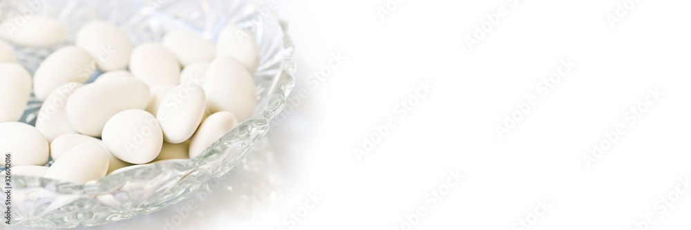 White dragees in a plate for baptism or wedding on white panoramic background White dragees in a plate for baptism or wedding on white panoramic background