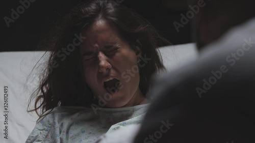 difficult childbirth and contractions in young woman, severe pain, loud scream, mother in labor in maternity ward gives birth to child or baby photo