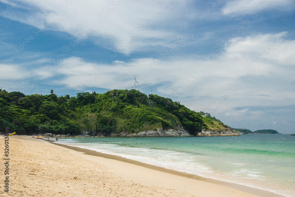 Phuket, Thailand - April 19, 2017. Sea beach with people and umbrellas, a large green hill and a wind generator.