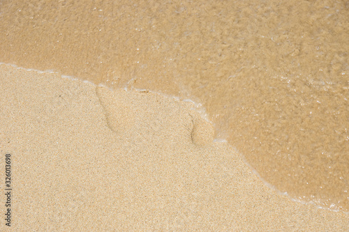 Canvas Print Traces of a man on a sandy beach and a sea wave erasing them.