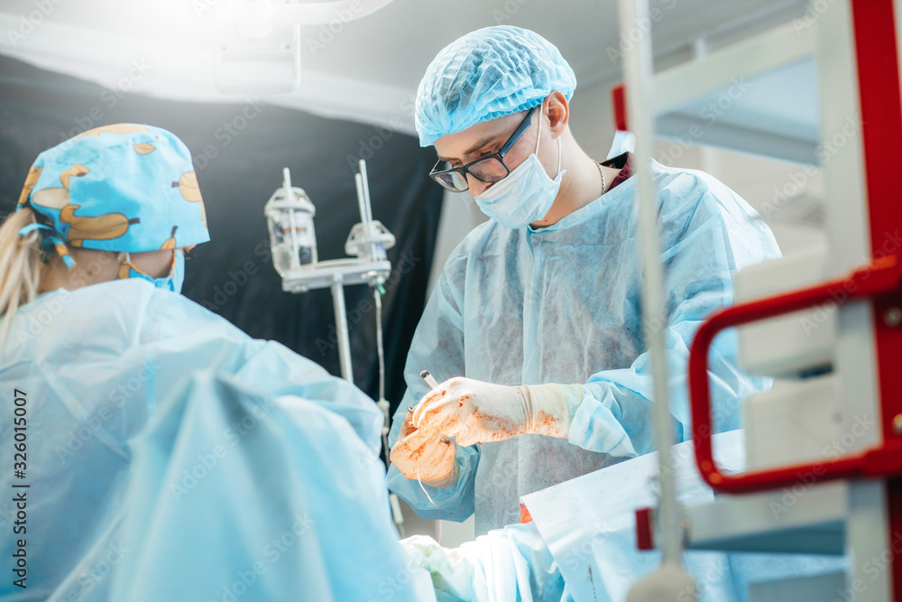 Surgeon performing surgery on breasts in hospital operating room. Surgeon in mask wearing surgical loupes during medical procedure. Surgeon performing surgery on breasts in hospital operating room. Surgeon in mask wearing surgical loupes during medical procedure.