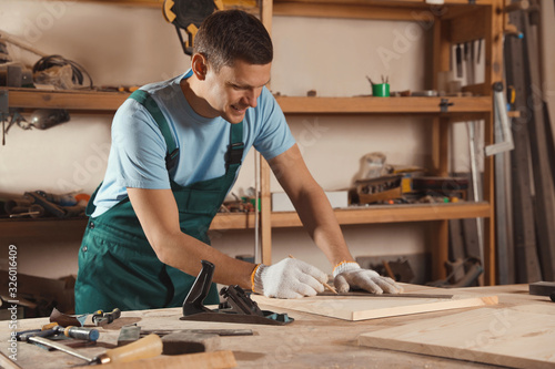 Картината върху платно Professional carpenter measuring wooden board in workshop