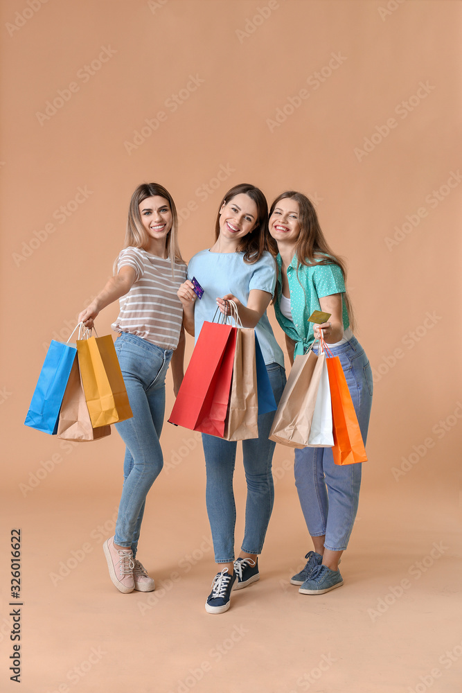 Young women with credit cards and shopping bags on color background