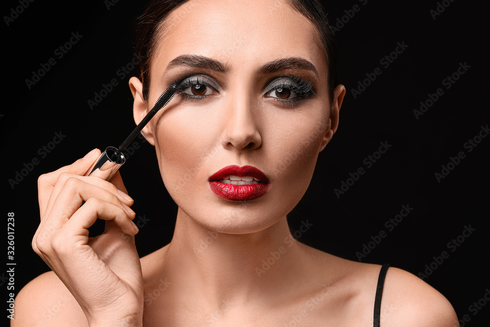Beautiful young woman applying makeup against dark background Beautiful young woman applying makeup against dark background