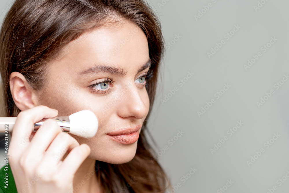 Close up portrait of a woman using makeup brush applying dry cosmetic tonal foundation on her face, makeup detail, copy space. Close up portrait of a woman using makeup brush applying dry cosmetic tonal foundation on her face, makeup detail, copy space.