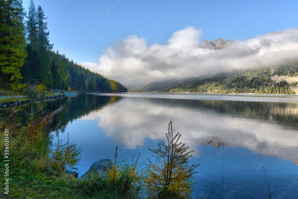Fototapeta premium Mountain lake at sunrise in autumn. Landscape with lake, gold sunlight, blue fog over the water, reflection, trees with colorful leaves