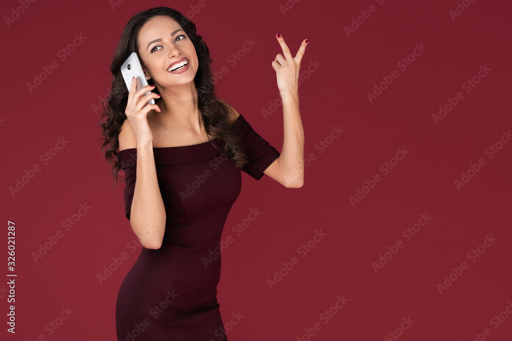 Amazed elegant young business woman in maroon dress use smartphone or mobile over red background. Amazed elegant young business woman in maroon dress use smartphone or mobile over red background.